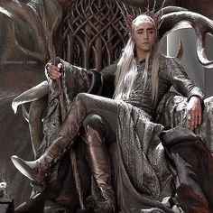 a man with white hair sitting on a throne next to a woman in silver dress