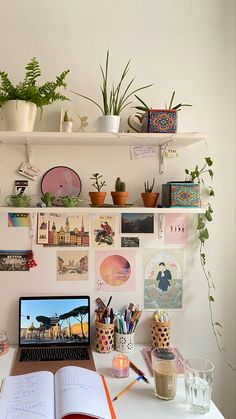 a laptop computer sitting on top of a white desk next to a plant filled wall