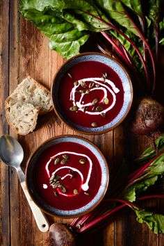 two bowls of beet soup on a wooden table with bread and radishes