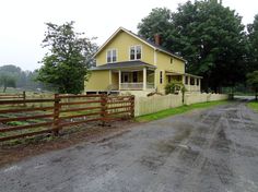 a yellow house sitting on the side of a dirt road next to a wooden fence