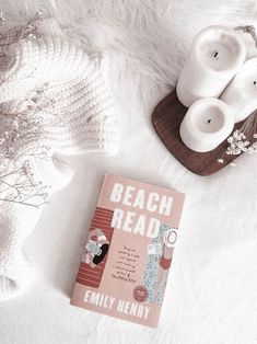 the book beach read is next to two candles on a white blanket and some flowers