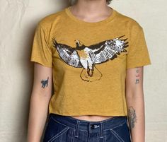 Our hand-drawn Red-Tailed Hawk design is printed in brown, white and orange on this super soft, raw-edge gold tee.   Available in  XS -2XL.  Runs a little small, order up for a slouchier fit. One model is an XS and wearing an XS. Other model is a medium/ large and wearing a large.  See size chart and message me with any questions.  Soft, lightweight 65%Poly/35%Cotton, sweatshop free. Our original, hand-drawn designs are printed on sweat-shop free clothing using environmentally conscious water-ba Hand Printed Relaxed Fit Short Sleeve Tops, Hand Printed Short Sleeve Tops With Relaxed Fit, Relaxed Fit Hand Printed Short Sleeve Tops, Hand Printed Crew Neck Top With Relaxed Fit, Gold Cotton Top With Relaxed Fit, Casual Gold Cotton Top, Relaxed Fit Hand Printed Crew Neck Top, Summer Streetwear Top Hand Printed, Gold Short Sleeve Top With Screen Print