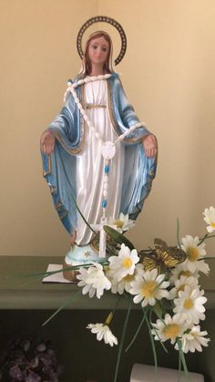 a statue of the virgin mary with daisies on a table