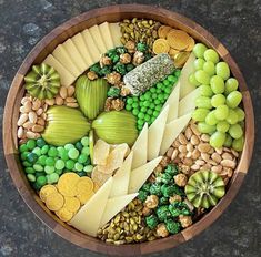 a wooden bowl filled with lots of different types of cheeses and vegetables on top of each other