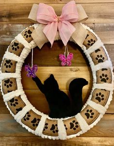 a wreath with a cat and butterfly hanging from it's side on a wooden wall