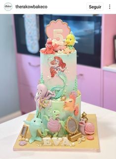 a little mermaid themed cake on top of a table with pink cabinets in the background