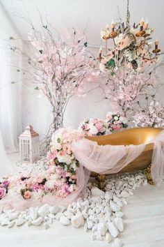 a bathtub surrounded by flowers, rocks and branches with a chandelier in the background