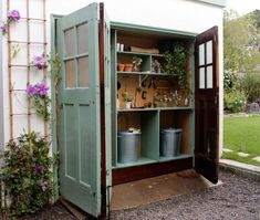 an outdoor storage shed with potted plants and gardening tools in the open door area