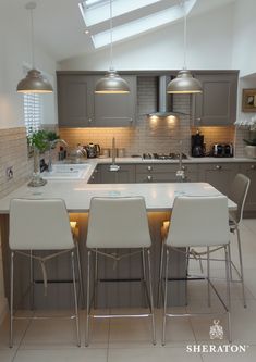 a kitchen with grey cabinets and white counter tops, three stools at the island