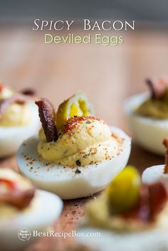 deviled eggs topped with bacon and olives on a wooden table next to other deviled eggs