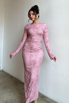 a woman in a pink dress is standing by a wall and posing for the camera