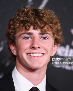 a young man wearing a suit and tie smiles at the camera in front of a black background