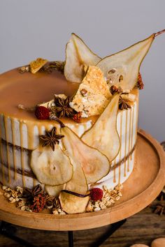 a cake decorated with apples and cinnamons on a wooden platter next to nuts