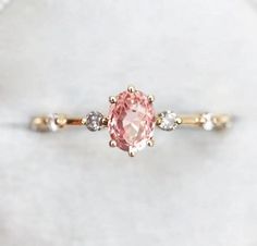 a pink diamond ring with three diamonds on the band and an oval shaped center stone