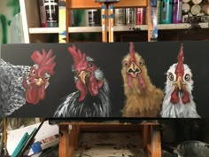 three roosters painted on an easel in front of paintbrushes and other art supplies