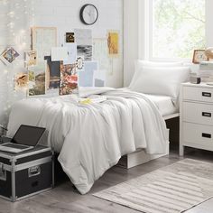 a bed with white sheets and pillows next to a suitcase on the floor in front of a window