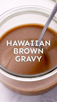 a glass bowl filled with brown gravy next to a spoon