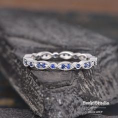 a wedding ring with blue sapphire stones on top of a stone slab in front of a rock