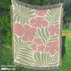 a pink and green flowered blanket hanging from a tree in the grass with trees behind it