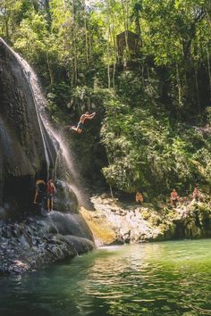 people are swimming in the water near a waterfall