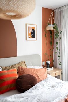 a bed with white sheets and pillows in a bedroom next to a plant hanging on the wall