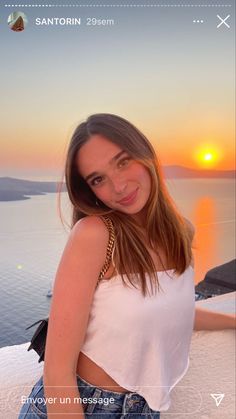 a woman posing for a photo in front of the ocean at sunset with her hand on her hip