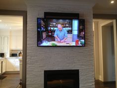 a man sitting in front of a flat screen tv mounted to a wall above a fireplace