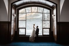 a bride and groom standing in front of a window looking out at the snow covered mountains