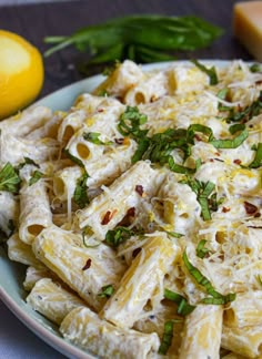 a plate full of pasta with cheese and herbs next to lemon wedges on a table