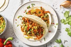 two tacos are sitting on a plate next to some peppers and onions, along with other ingredients