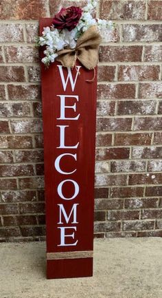 a red welcome sign with flowers on it sitting in front of a brick wall that says welcome