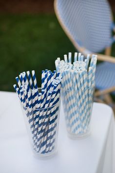 several blue and white striped paper straws in cups on a table outside with chairs