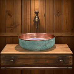 a copper and blue bowl sitting on top of a wooden table next to a faucet