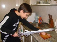 a young boy is holding a large pair of scissors in his hand while standing at the kitchen sink