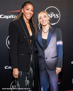 two women standing next to each other in front of a red carpet with the caption capital