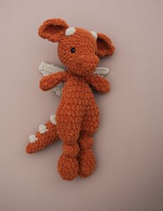 an orange crocheted stuffed animal laying on top of a gray surface with white wings