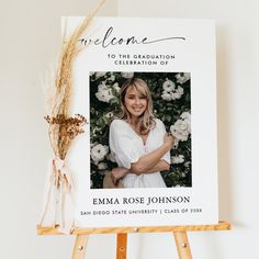 an easel with a photo and flowers on it next to a sign that reads, welcome to the graduation