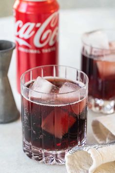 two glasses filled with coke and ice on top of a table next to a can