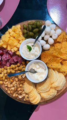 a platter filled with crackers, olives, pita chips and dip