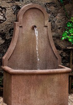 a fountain with water coming out of it in front of a stone wall and green plants