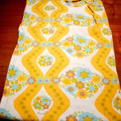 a yellow and blue flowered bed spread on top of a wooden floor next to a pillow