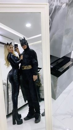 two people dressed as batman and catwoman taking a selfie in front of a mirror