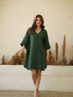 "Style Tip: Flowy linen dress, with draped kaftan sleeve, a modest V neckline, and comes fully lined with a soft cotton voile. The dress can also be worn as a blouse or a cover-up. Fabric: Organic Linen Lining: Organic Cotton Fit Type: Fluid fit with kaftan sleeve Length: 40\" or 100cm and can be made longer or shorter. Care: Hand/Machine wash, Cool Rinse, Drip Dry In Shade, Flat Iron, Do not Bleach Model Note: The model is wearing size 'S' in color 'Bottle Green' and is 5'8 or 172cm" Casual V-neck Linen Dress For Brunch, Casual Green Linen Dress For Beach, Spring Linen V-neck Kaftan, Green Linen Dress With Relaxed Fit For Vacation, Green Relaxed Fit Linen Beach Dress, Green Relaxed Fit Linen Dress For Vacation, Oversized 3/4 Sleeve Summer Dress, Shift Linen Dress For Spring Beach Occasions, Green Bohemian Linen Dress For Vacation