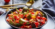 a black bowl filled with vegetables on top of a table next to utensils