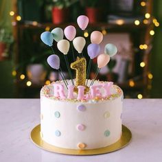 a birthday cake decorated with balloons and the number one on top is pink, blue, yellow, and white