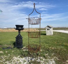 an iron basket and candle holder stand in the middle of a grassy field with a small shed in the background