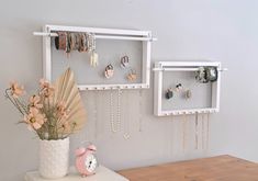 a vase with flowers and jewelry hanging from it's sides next to a wall mounted shelf