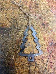 a metal christmas tree ornament hanging from a string on a piece of wood