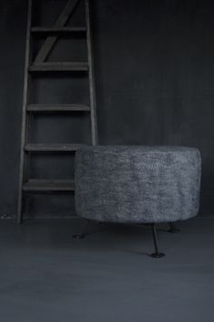 a ladder leaning up against a wall next to a gray chair and ottoman in a dark room