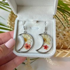 𝐑𝐄𝐀𝐋, 𝐏𝐑𝐄𝐒𝐒𝐄𝐃 𝐅𝐋𝐎𝐖𝐄𝐑𝐒 ✨    These earrings are made with real pressed flowers, perfectly preserved within resin. Their color and beauty will live on forever!       This is the perfect, 𝐭𝐡𝐨𝐮𝐠𝐡𝐭𝐟𝐮𝐥 gift for any plant lover, moon enthusiast, or spiritual girlie in your life.          𝐒𝐩𝐞𝐜𝐢𝐟𝐢𝐜𝐚𝐭𝐢𝐨𝐧𝐬: Material: Stainless steel, resin, real daisies.    Size: Approximately 1 inch in length.    Closure: Stainless steel hook.          𝐖𝐇𝐘 𝐘𝐎𝐔 𝐒𝐇𝐎𝐔𝐋𝐃 𝐂 Bohemian Style Resin Flower Earrings As Gift, Hypoallergenic Flower-shaped Resin Jewelry, Hypoallergenic Moon Shaped Earrings Gift, Hypoallergenic Moon-shaped Earrings For Gift, Resin Flower Earrings With Pressed Flowers, Round Resin Earrings With Pressed Flowers, Silver Pressed Flowers Earrings For Gift, Resin Round Birth Flower Earrings, Round Resin Birth Flower Earrings